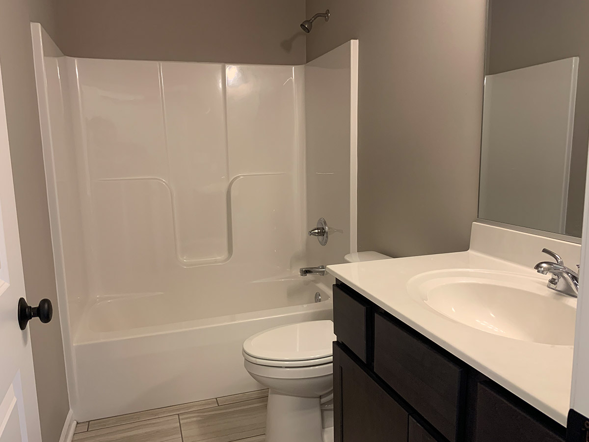 The Stockton bathroom sink with dark vanity, shower, toilet, and tile floor