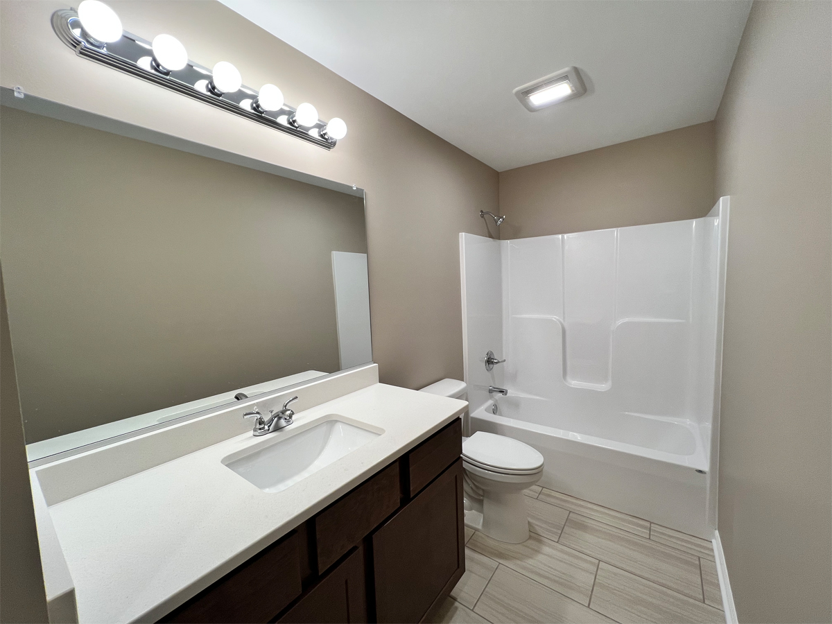 The Redbud main bathroom with vanity, toilet and fiberglass shower