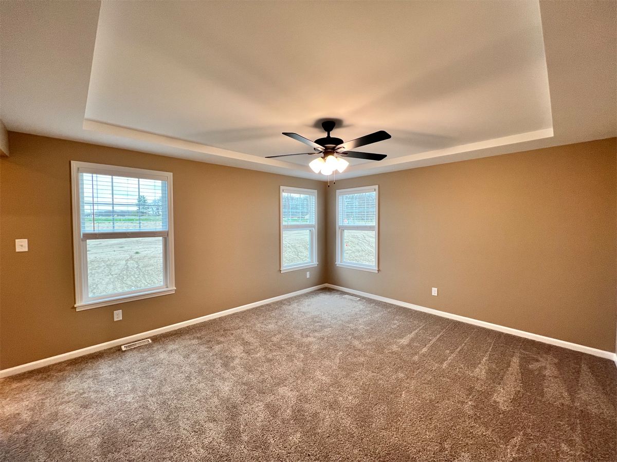 The Redbud master bedroom with boxed ceiling, ceiling fan, carpet and windows