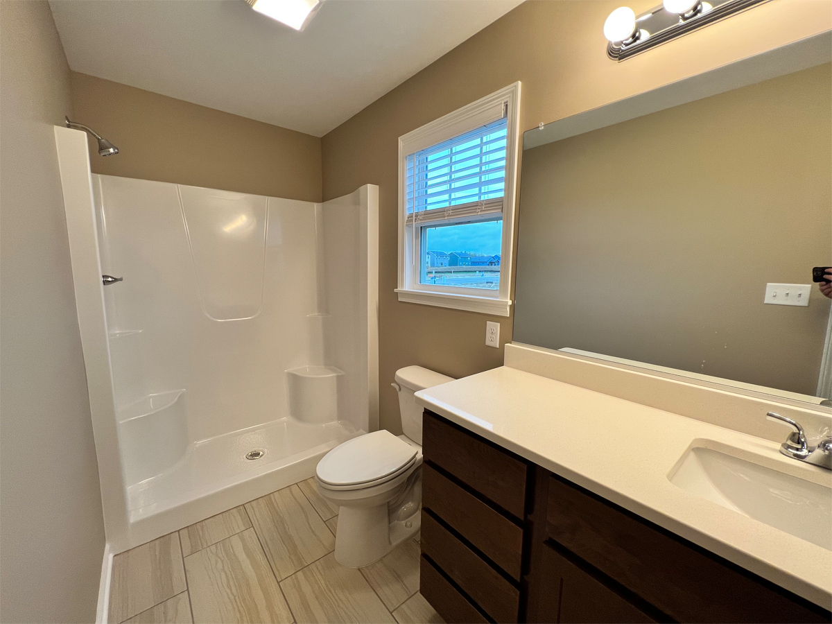 The Redbud master bathroom with vanity, mirror, fiberglass shower and ceramic floor