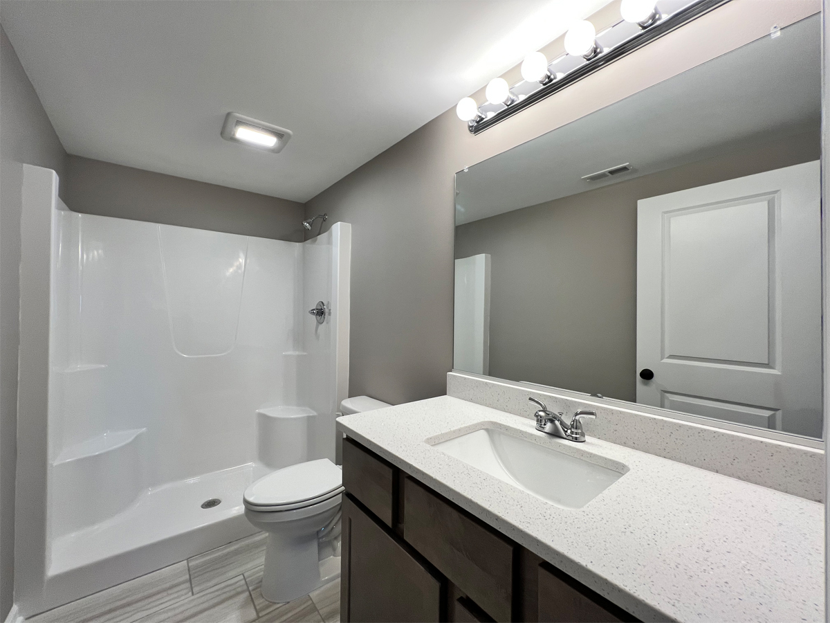 The Revere lower level bathroom with vanity, toilet and fiberglass shower