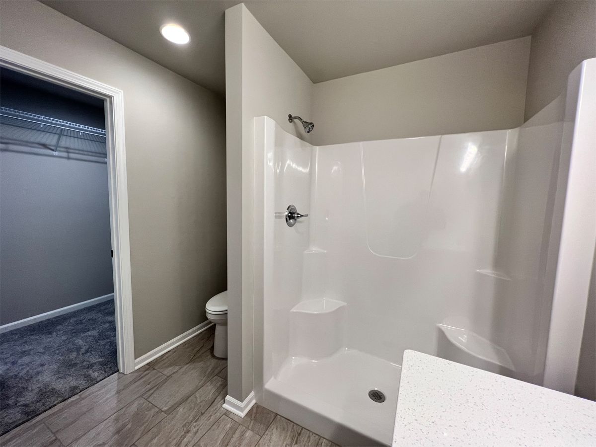 The Washington master bathroom fiberglass shower, toilet and entrance to walk in closet