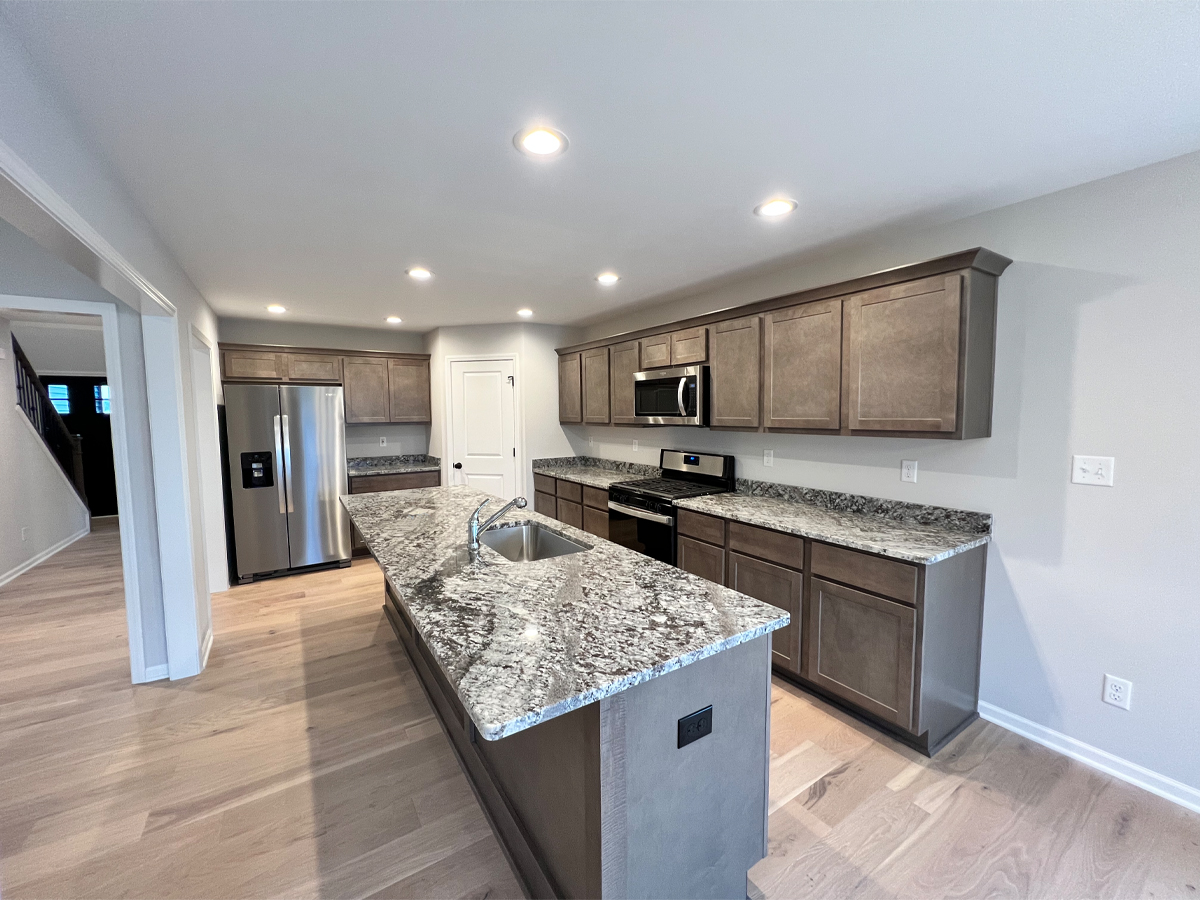 The Walton kitchen with brown cabinets, hardwood floors and granite countertops