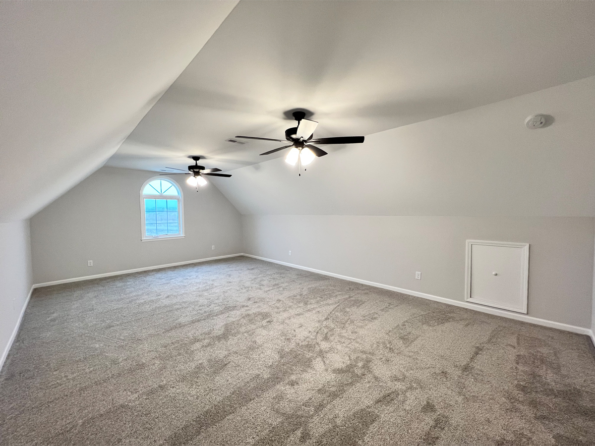 The Walton large bonus room with two ceiling fans, window and carpet